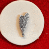 Silver feather pin on red background.