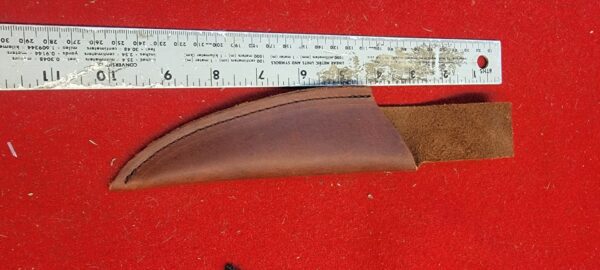Knife sheath and ruler on red surface.