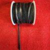 Spool of black ribbon on red fabric.