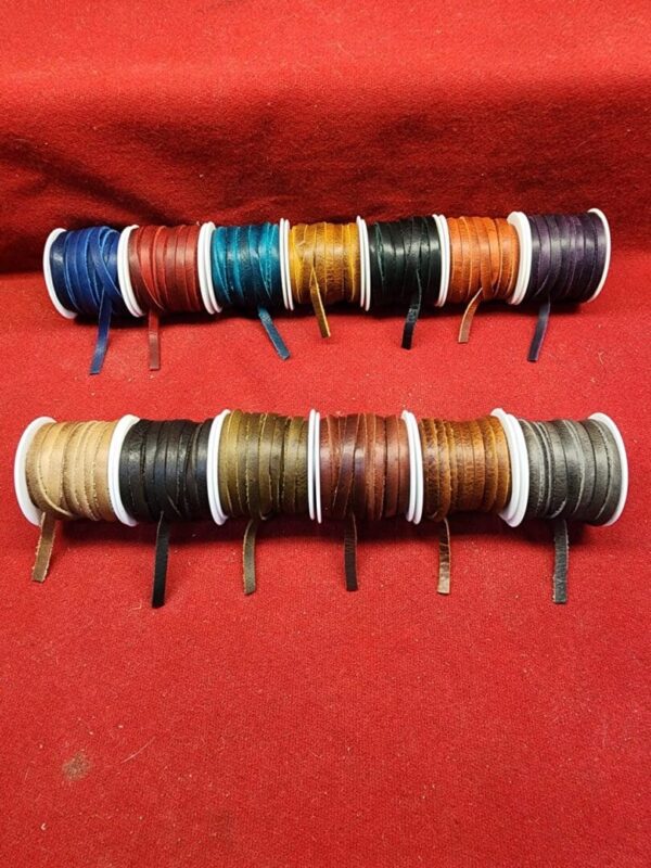 Colorful leather cords on spools, red background.