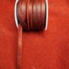 Brown leather ribbon on spool, red background.