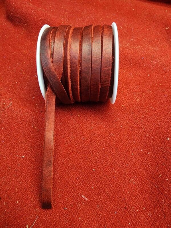Brown leather ribbon on spool, red background.