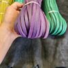 Hand holding purple leather strips, various colors.