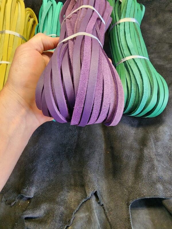 Hand holding purple leather strips, various colors.