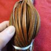 Bundles of brown leather strips in hand.
