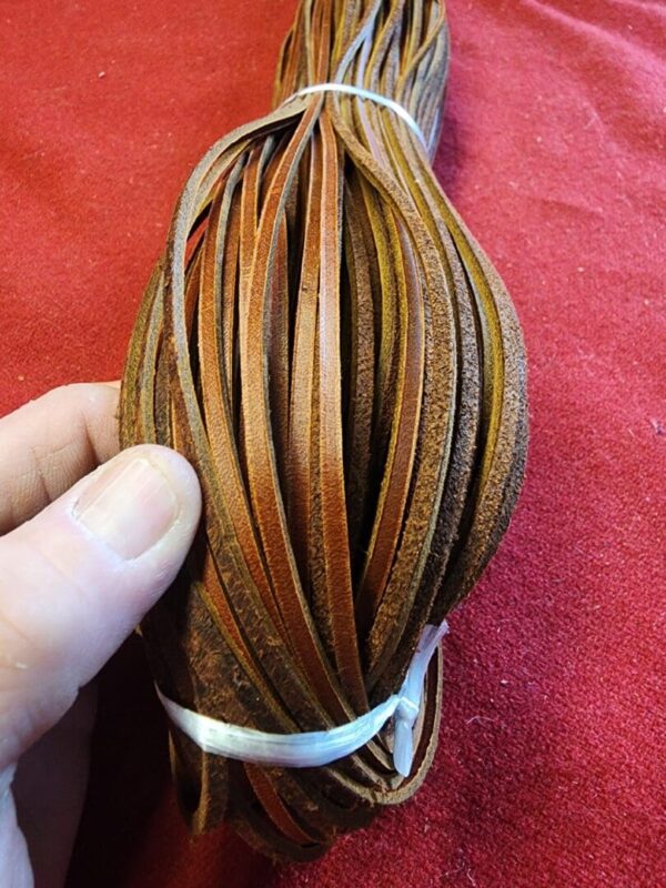 Bundles of brown leather strips in hand.