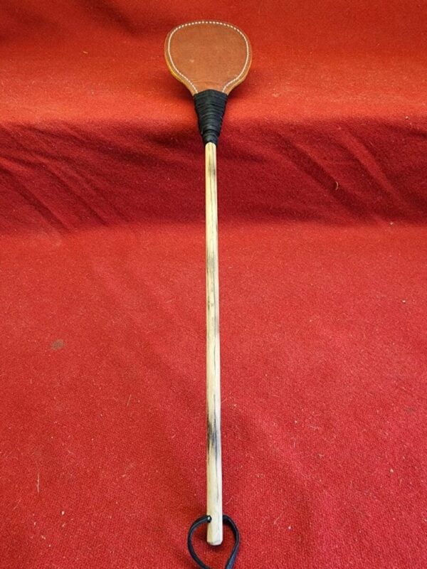 20240629_134444 Wooden paddle with leather handle on red background.