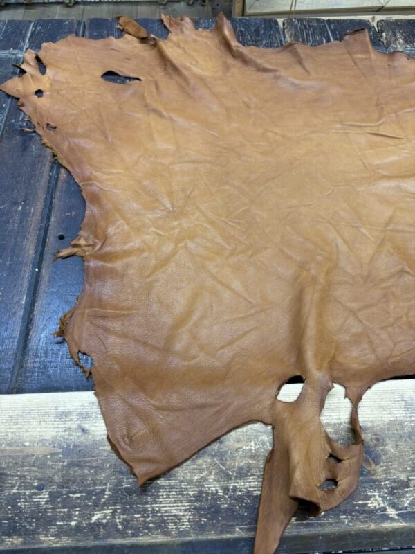 Tanned leather hide on wooden surface.