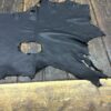 Torn black leather piece on wooden surface.