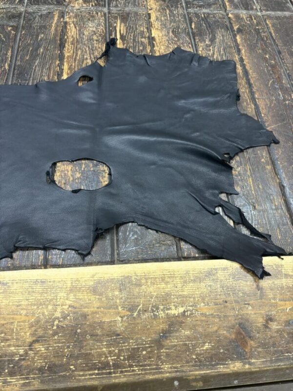 Torn black leather piece on wooden surface.
