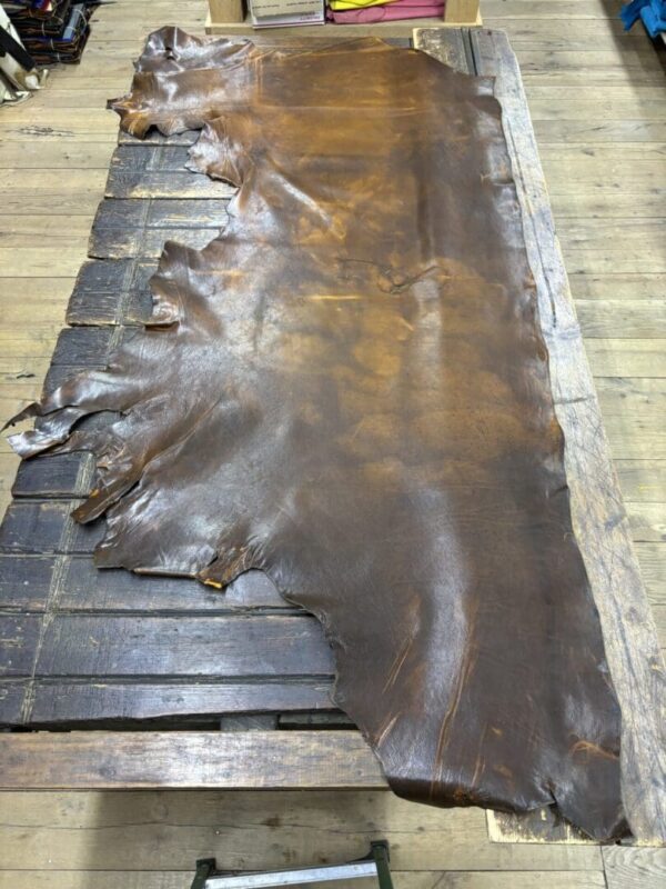 Brown leather hide laid on wooden surface.
