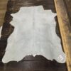Light gray cowhide rug on wood floor.