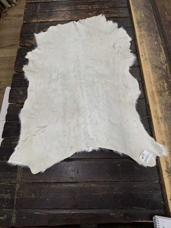 White goat skin fur rug on wood floor.